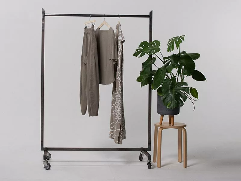 Drei olivfarbene Kleidungsstücke an einer Kleiderstange neben einer Monstera