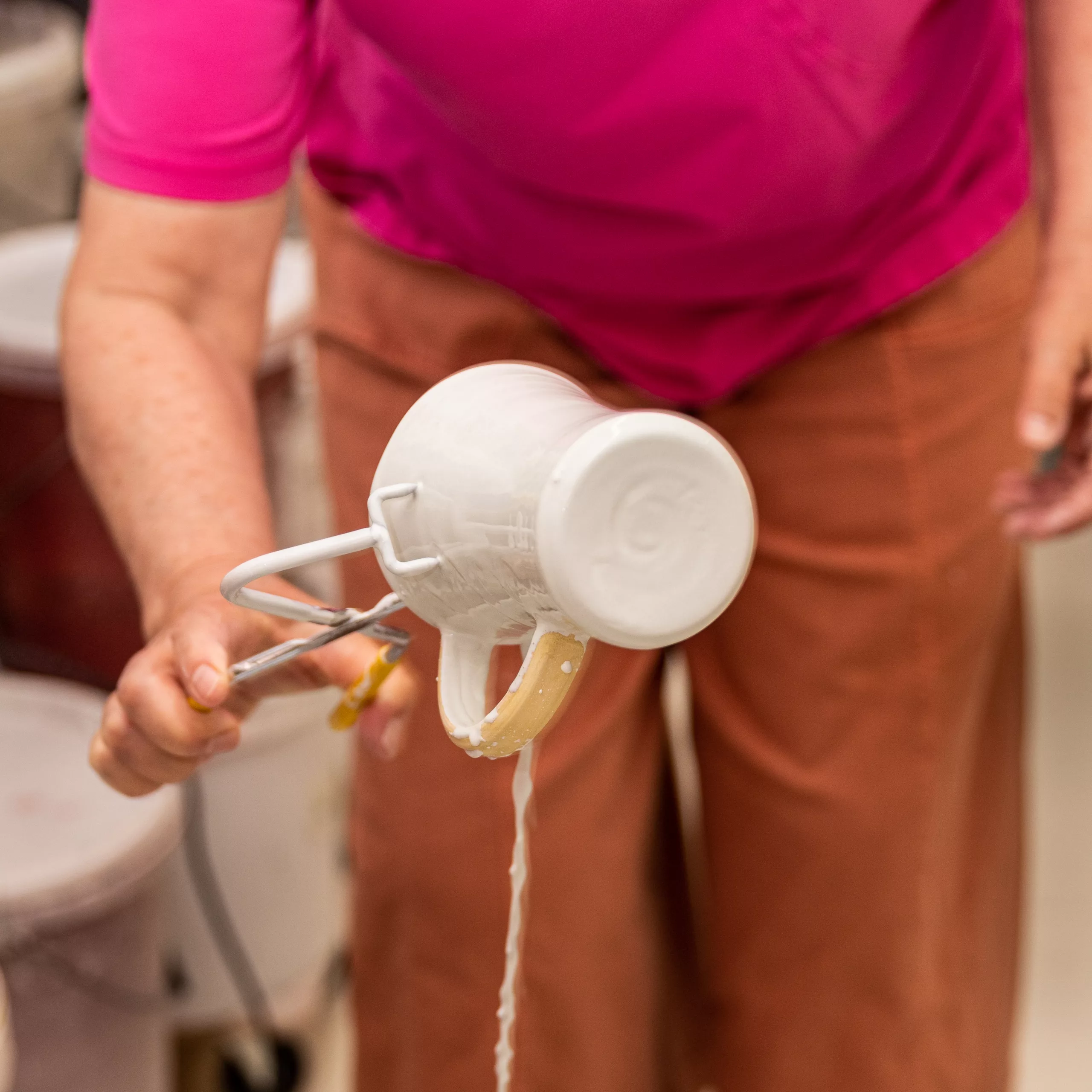 A cup is dipped into white glaze with tongs
