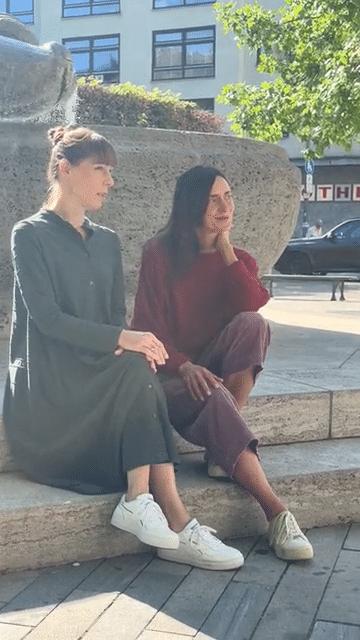 Iris und Julia sitzen am Rand eines Brunnens in der Sonne