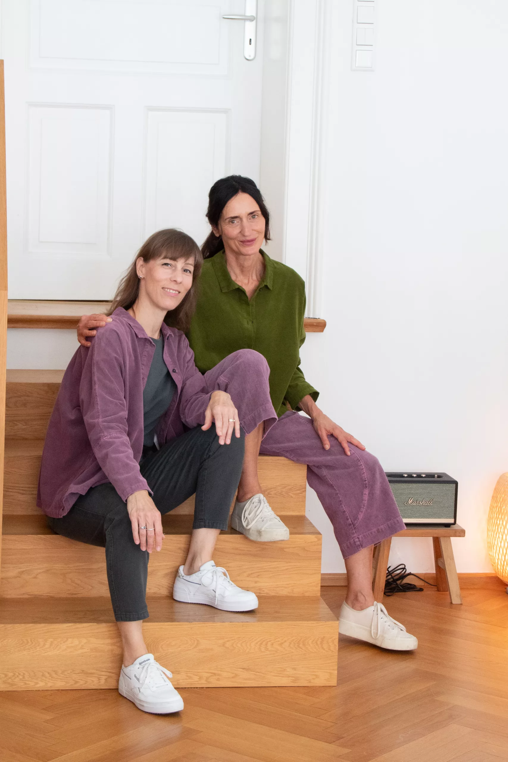 Iris und ihre Kollegin Julia sitzen auf einer Holztreppe