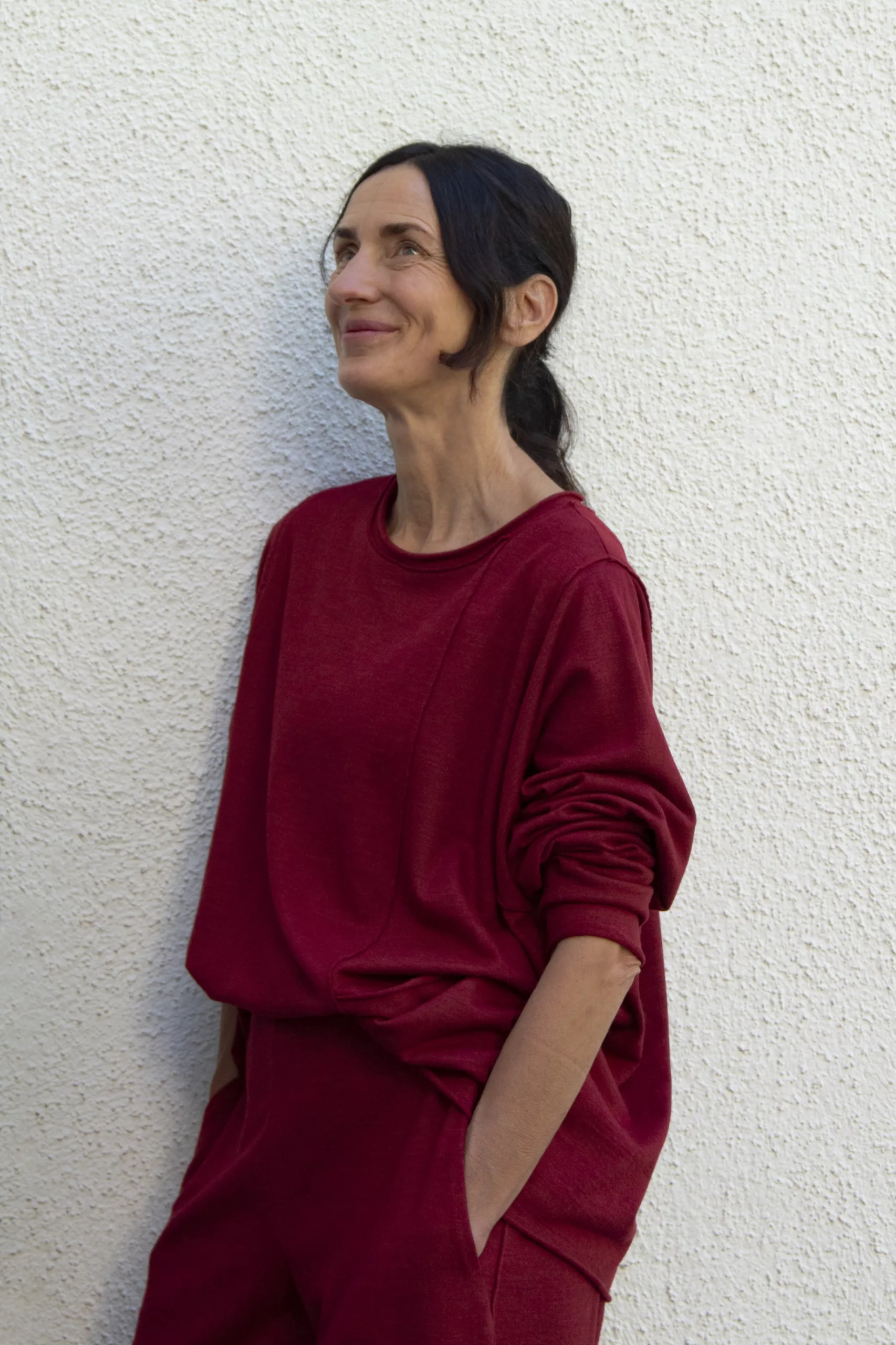 Iris in rotem Zweiteiler lehnt an einer weißen Wand