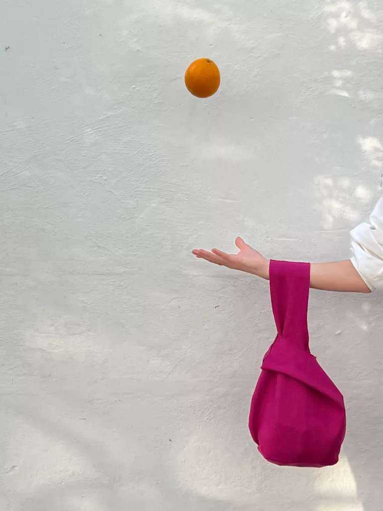 Pink knot bag on a wrist, an orange tossed above it