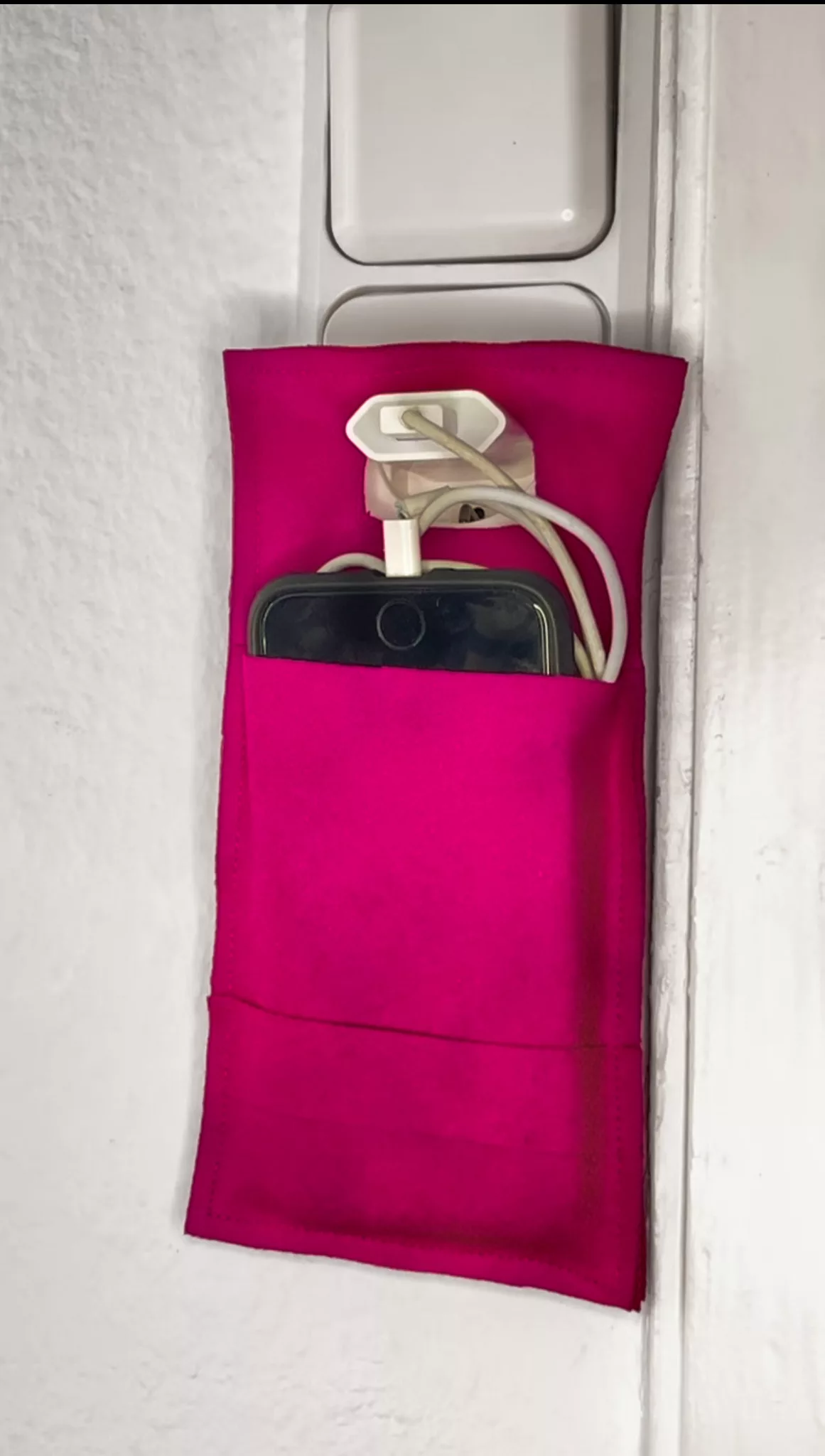 Magenta phone pouch with phone and charging cable hanging from a socket