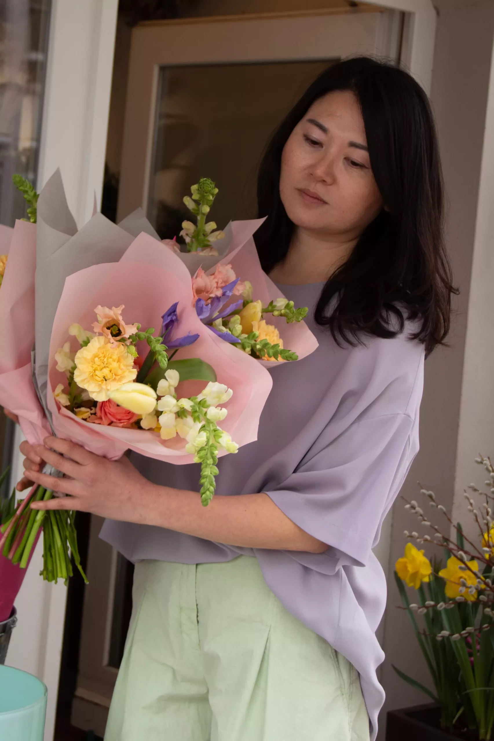 Ji mit einem in rosa Papier gewickelten Blumenstrauß