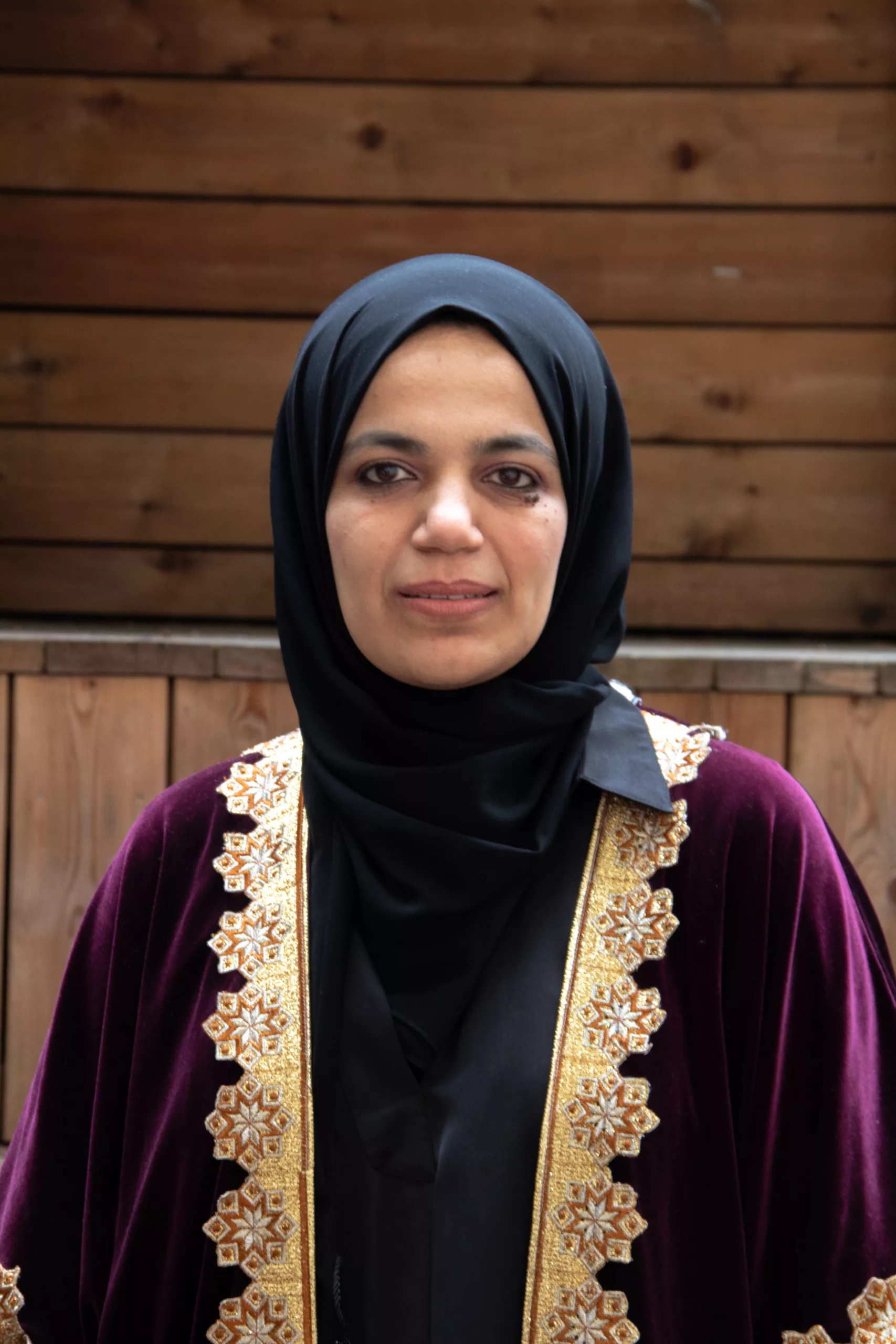 Woman in a black hijab and a burgundy velvet robe with gold embroidery
