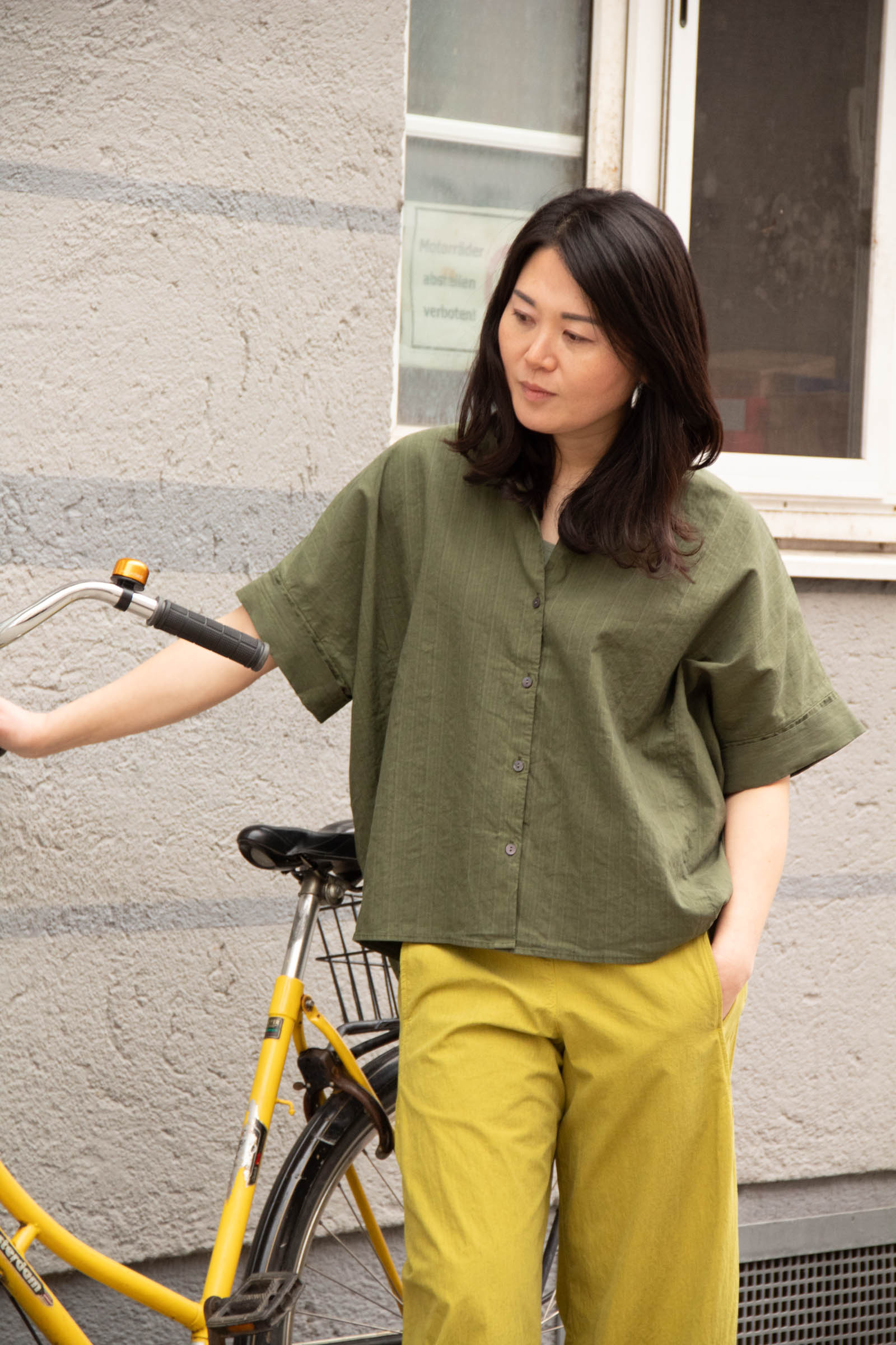 Ji mit gelbem Fahrrad vor einer Hauswand