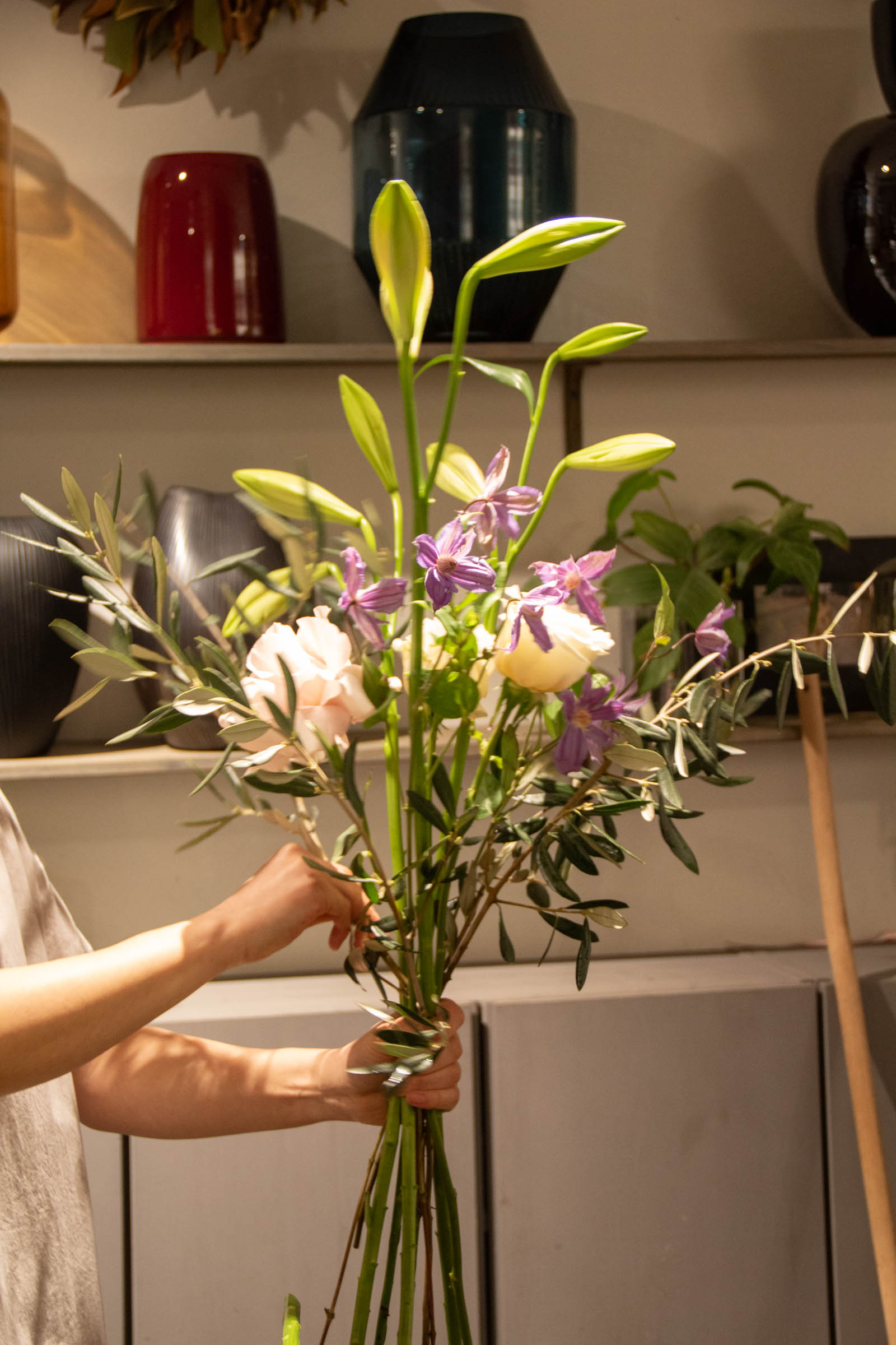 Hände binden einen Strauß mit Lilien, Rosen und Klematis