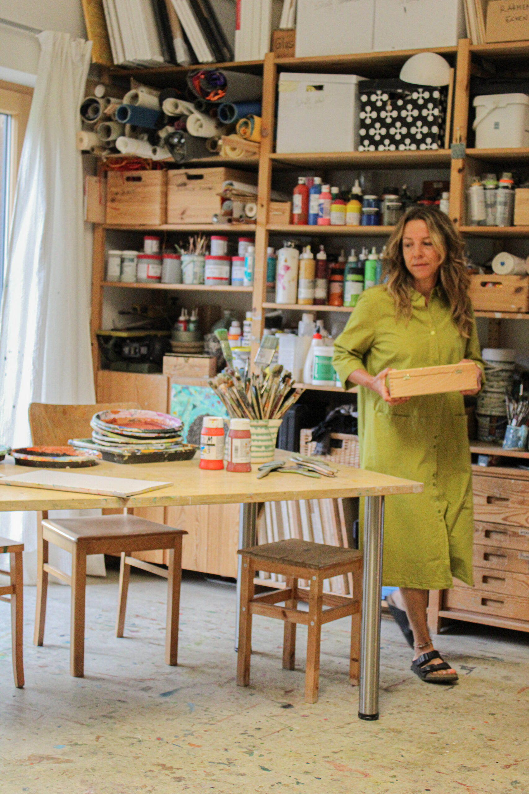 Marlene trägt eine Holzkiste durch ihr Atelier