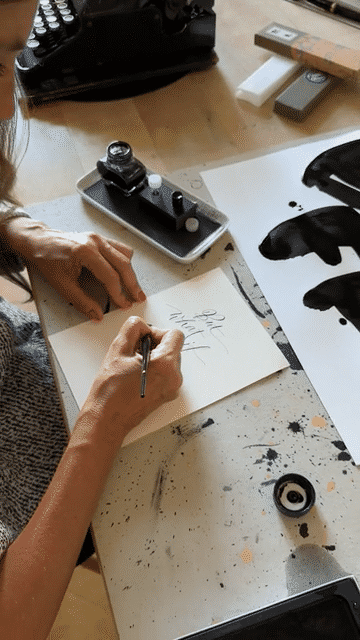 Hand schreibt Kalligrafie mit der Feder neben einem Tintenglas