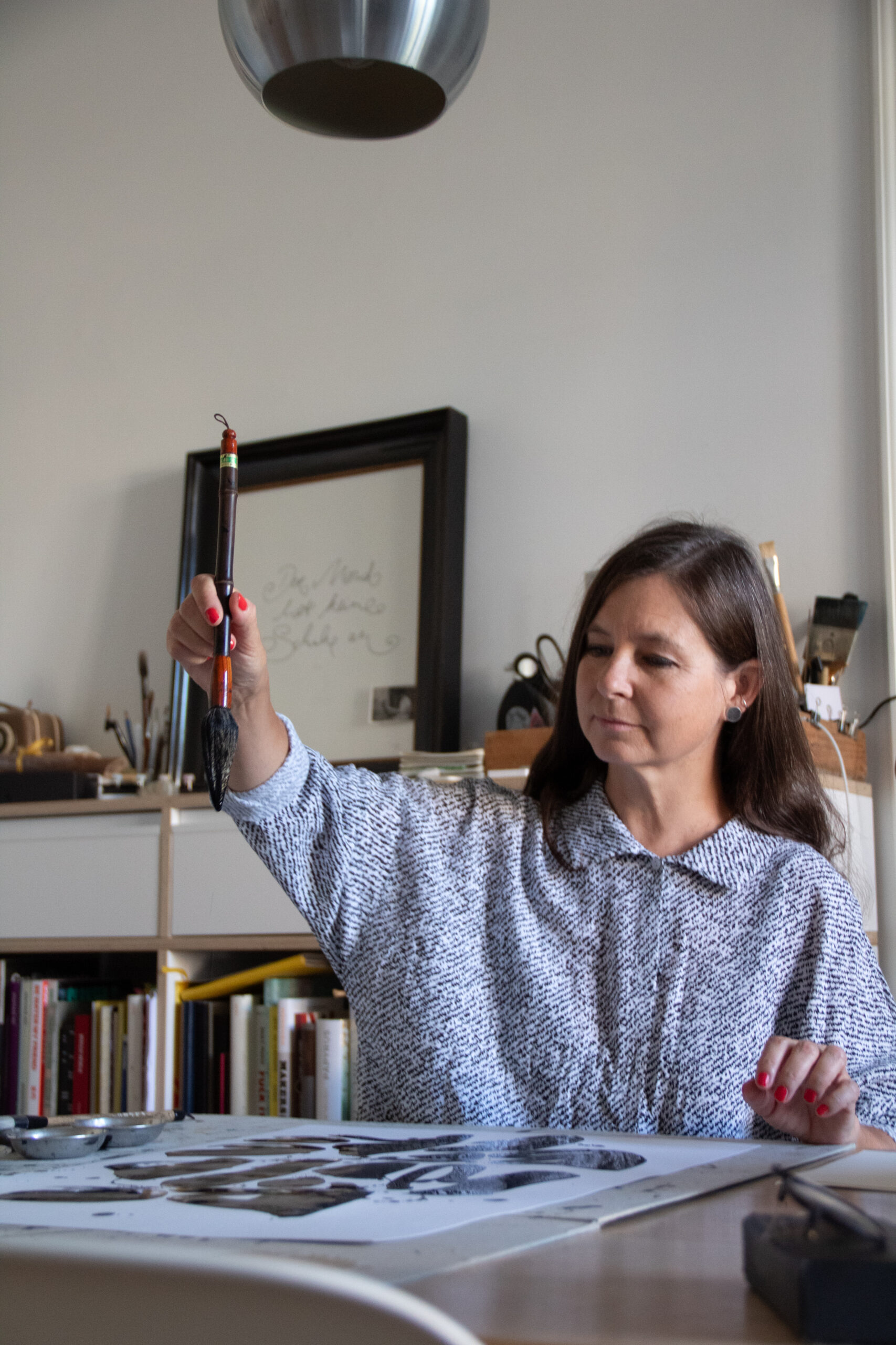 Petra hält einen Pinsel am Schreibtisch hoch