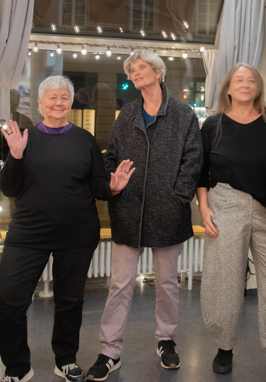 Drei Frauen winken vor einem Fenster mit Lichterkette
