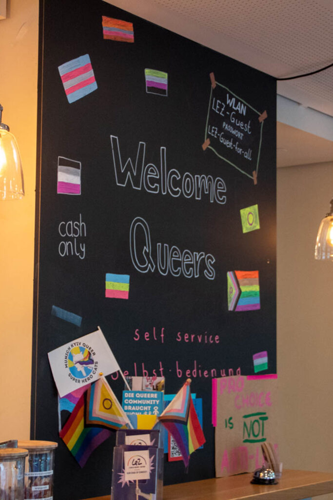 Blackboard reading Welcome Queers with pride flags