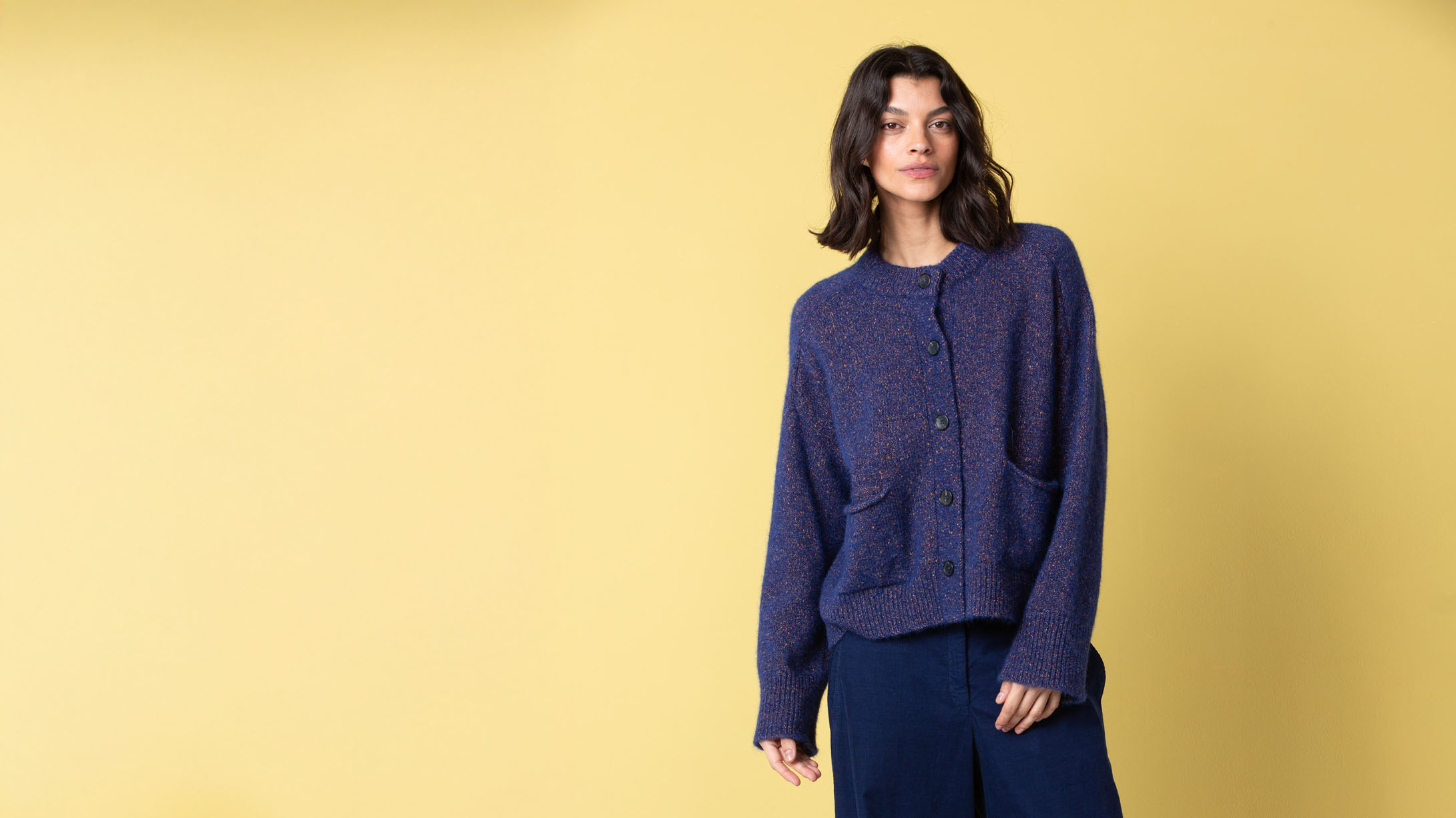 Model in a blue cardigan against a yellow background
